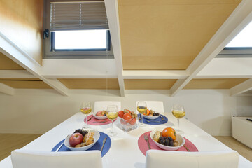 Studio living room with white rectangular dining table with lots of assorted fruit, vaulted ceilings and skylights