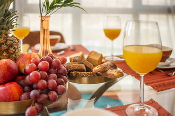 Centerpiece with tray of fresh fruit, bunch of grapes, lots of muffins and sweets, decorative vase, red apples, ripe plums and glasses of orange juice