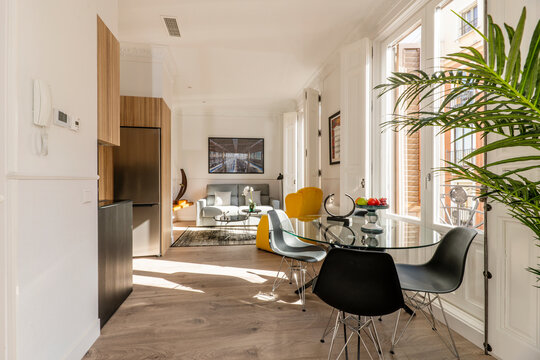 Living room of studio apartment with open kitchen with round glass table, black resin chairs and balconies to the street