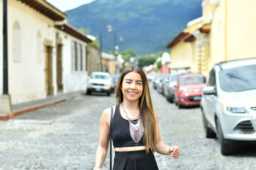 Mujer joven latina y sonriente parada en medio de la calle en Antigua Guatemala. Concepto de viaje y vacaciones. - obrazy, fototapety, plakaty