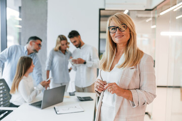 Woman in glasses standing in the front of her colleagues. Group of professional business people is in the office