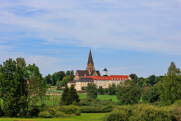 The church tower of St. Ottilien Monastery in Bavaria between forests and meadows under white blue sky