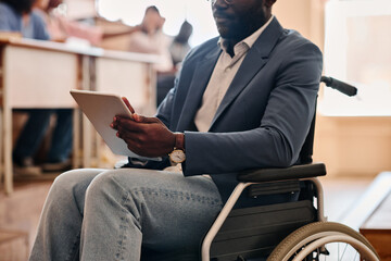 Close-up of African teacher with disability sitting on wheelchair and using digital tablet during...