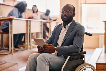 Portrait of African teacher with disability sitting on wheelchair using digital tablet at lecture at university