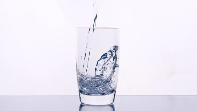 Pouring drinking water. Close up pouring purified fresh clean drinking water into glass, water splashing in glass on white background, soft focus 4K. Concept of drinking, health, nature