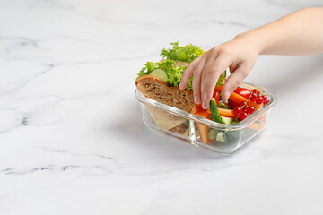 Girl taking, reaching a sandwich, toasts, vegetables, snack. Container, glass box with take away school healthy food. School lunch.