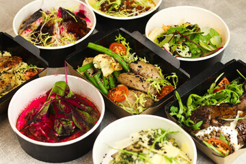 Delivery of healthy food in takeaway restaurants for daily nutrition. Set of containers with everyday meals - meat, fish, vegetables and law fat snacks on a gray background.