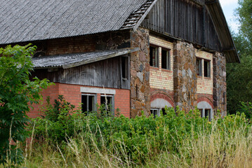 old abandoned building in nature park overgrown with green grass on cloudy day in mid-summer with broken windows