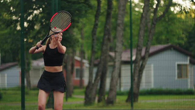 young woman is playing tennis in outdoor court in nature, active rest in summer weekend