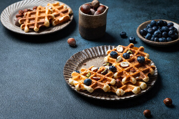 Belgian waffles with honey and fresh berries blueberry and hazelnut on dark background. Delicious dessert. Copy space. Space for text. Delicious breakfast.