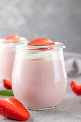 Strawberry mousse in a glass jar on a gray concrete background with whipped cream, fresh berries and mint leaves. Delicious summer dessert.