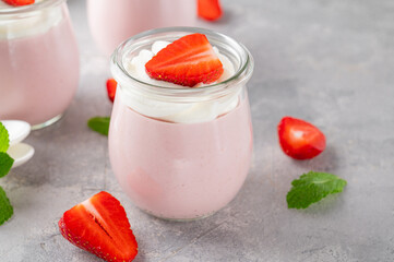 Strawberry mousse in a glass jar on a gray concrete background with whipped cream, fresh berries and mint leaves. Delicious summer dessert.