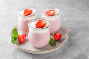 Strawberry mousse in a glass jar on a gray concrete background with whipped cream, fresh berries and mint leaves. Delicious summer dessert.
