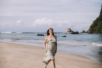 Fototapeta na wymiar Young woman in dress walking alone on the beach in tropical nature