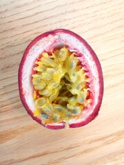 Half passion fruit showing yellow seeds and pink skin lying on wooden table