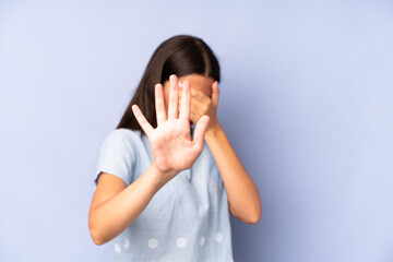 hispanic pretty woman covering face with hand and putting other hand up front to stop camera,...
