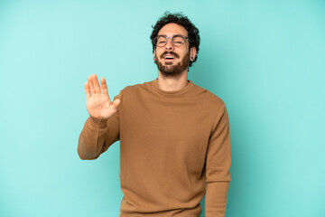 young bearded man smiling happily and cheerfully, waving hand, welcoming and greeting you, or...