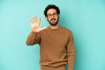 young bearded man smiling and looking friendly, showing number five or fifth with hand forward,...