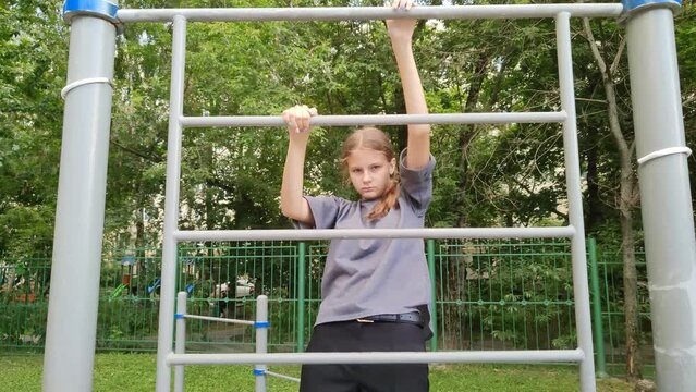 Teenage girl is stands on Swedish wall on outdoor playground. Schoolgirl is engaged in sports field. Active lifestyle. Children's health. Playground on street near school or home. Close-up