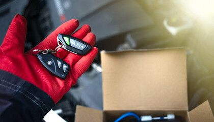 Installing an anti-theft alarm in the car.A gloved hand holds an alarm keychain against the open hood of a car.