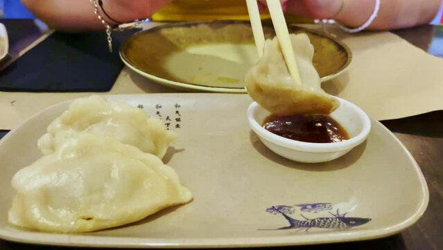 Chica cogiendo con palillos de madera una gyoza y mojando en salsa de soja en un resturante japones 