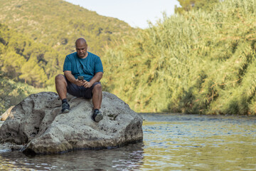 Man sitting on a rock in the river, using a phone.