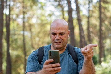 Portrait of a male hiker lost in the woods, he uses the phone to guide himself and find the way.
