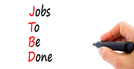 JTBD jobs to be done symbol. Concept words JTBD jobs to be done on yellow paper on a beautiful white background. Businessman hand. Light bulb. Business and JTBD jobs to be done concept. Copy space.