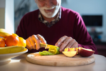 Senior man eating fruits in the kitchen on a sunny day