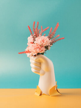White plastic hand holding pink flowers on a two tone background. Gift, present conceptual backdrop.