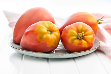 Bull heart tomatoes on plate on white table.