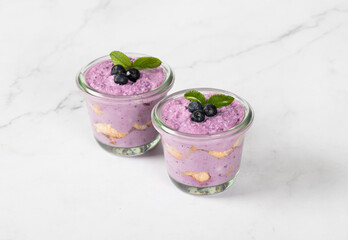 Italian dessert. Blueberry tiramisu, with mascarpone cottage cheese, cream and pieces of sponge cookies, in a glass. Light background