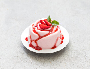 Italian dessert. Strawberry Panna Cotta with sauce, in the shape of a rose, on a plate. Light grey background