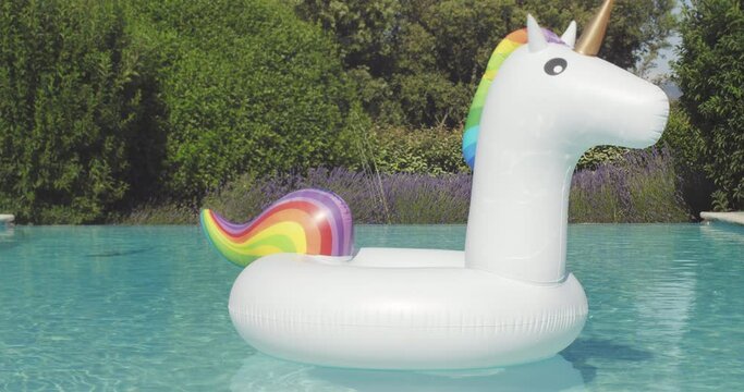 Inflatable colorful white unicorn at the swimming pool. Vacation time in the swim pool with plastic toys.Splash Water in swimming pool with sun reflection.Relaxation and fun. High quality 4k footage
