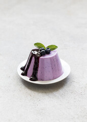 Blueberry Panna Cotta with sauce on a plate. Light gray background