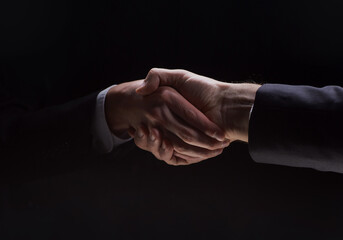 Photo of two men in suits shaking hands on a black background