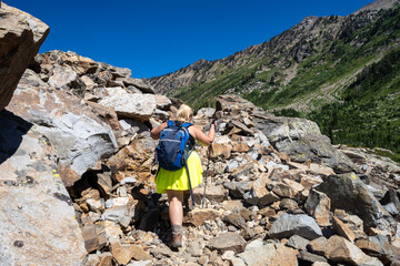 Woman hiker wearing a backpack and using trekking poles makes her way across scree along the Lake...
