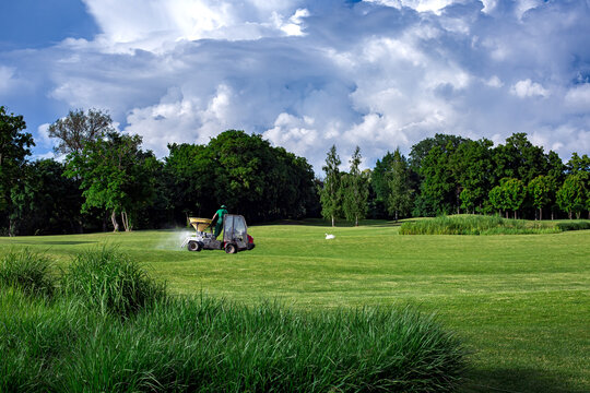transport specialized equipment for fertilization and lawn care on a golf course, gardening supplying plants with nutrients on a hilly landscape on a sunny day with clouds on the sky.