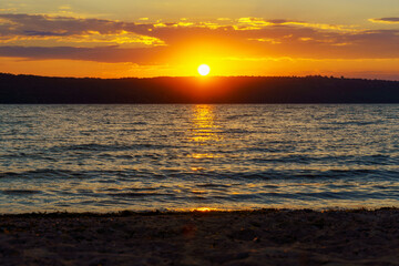 sunset over the lake, bright sun reflected in the waves, glare on the water, beautiful summer landscape