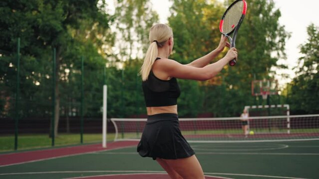 blonde female tennis player is hitting ball on court, slow motion shot, rear view on sexy figure