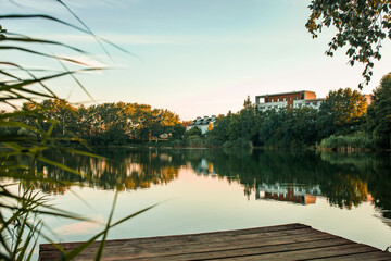 Colorful summer park and lake view, wooden pier. Summer evening. Photo. Nature. An empty wooden pier and a green tree on the background of the park.