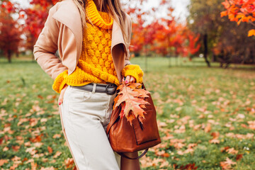 Close up of stylish woman holding purse wearing yellow sweater in autumn park. Fall female clothes,...