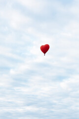 Red hot air balloon in shape of heart is landing on the green field