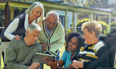 African nurse using tablet with two elderly retired couples outdoor in the rehab hospital garden. Happiness, rehabilitation and retirement concept