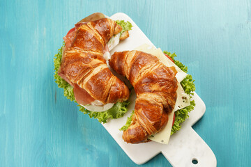 two lye croissant sandwiches with iberian ham, tomato slices, lettuce and cheese on marble board on...