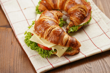 two lye croissant sandwiches with iberian ham, tomato slices, lettuce and cheese on marble board on...