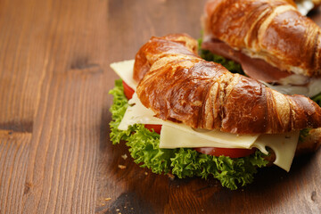 two lye croissant sandwiches with iberian ham, tomato slices, lettuce and cheese on marble board on wooden background