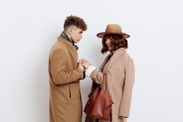 a beautiful, pleasant couple, a man and a woman are standing on a light background holding hands, dressed in warm brown autumn coats. Horizontal Studio Photography
