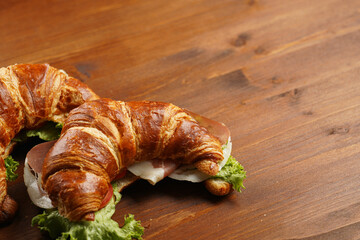 two lye croissant sandwiches with iberian ham, tomato slices, lettuce and cheese on marble board on...