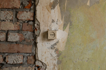 Old wall with a socket under renovation. Brickwork and old plaster without wallpaper. The textured background of a vintage wall. Abstract background with construction concept.